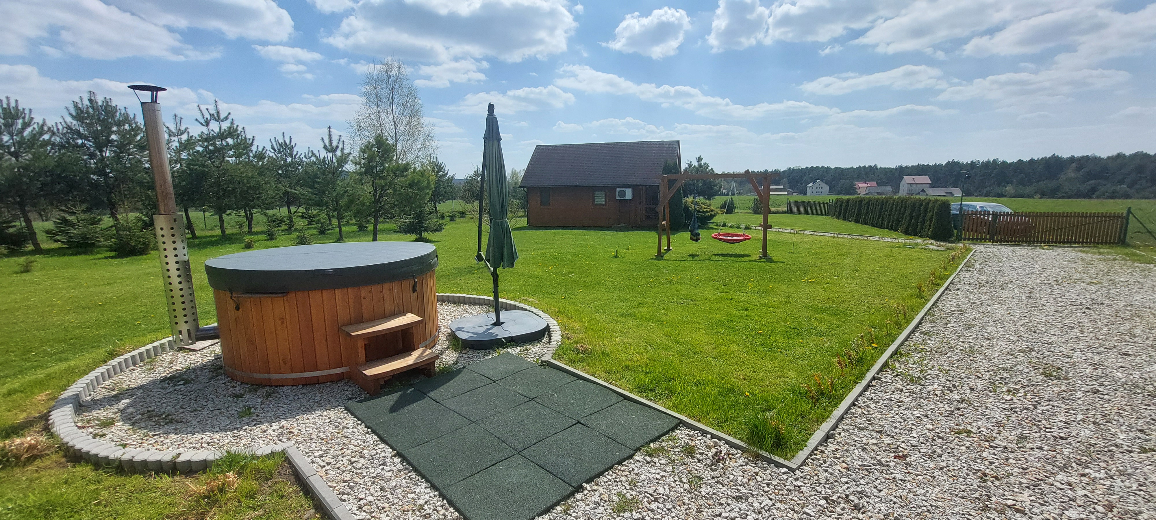 drewniana huśtawka na terenie agroturystyki, widoczna ścieżka z kamienia oraz stodoła